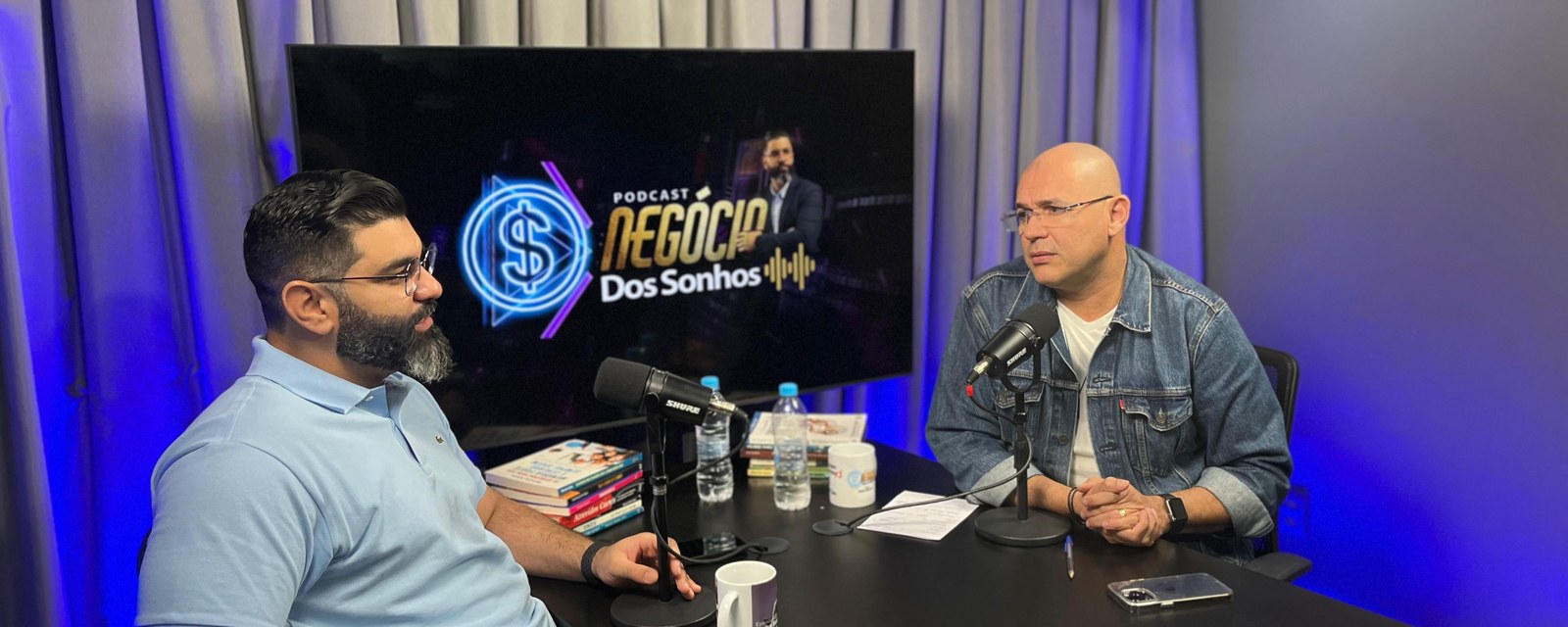 Two podcast speakers recording with studio microphones at a production desk